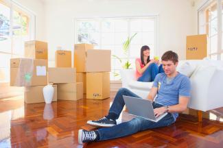 Couple sitting among moving boxes with laptop